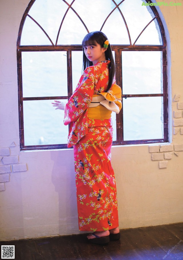 A woman in a red kimono standing in front of a window.