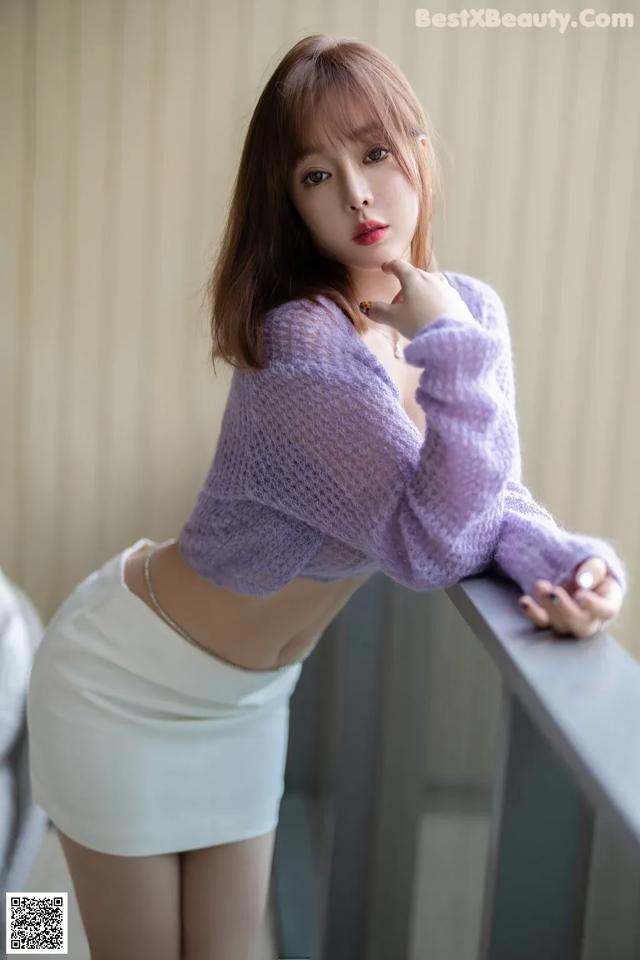 a woman in a purple sweater and white skirt posing for a picture