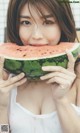 A woman holding a slice of watermelon in front of her face.