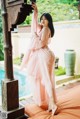 A woman in a pink dress standing next to a pool.