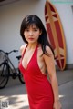 A woman in a red dress standing next to a surfboard.