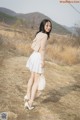 A woman in a white skirt and heels standing on a dirt road.