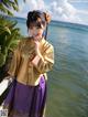 A woman in a yellow and purple dress standing by the water.