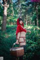 A woman in a red riding hoodie holding a basket in the woods.